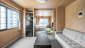 A modern living room with a sofa, a coffee table, and a kitchen area visible through an open door. - MITTO (Sapporo)