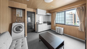 A compact hotel room with a washing machine, kitchenette, sofa, and a large window with curtains. - MITTO (Sapporo)
