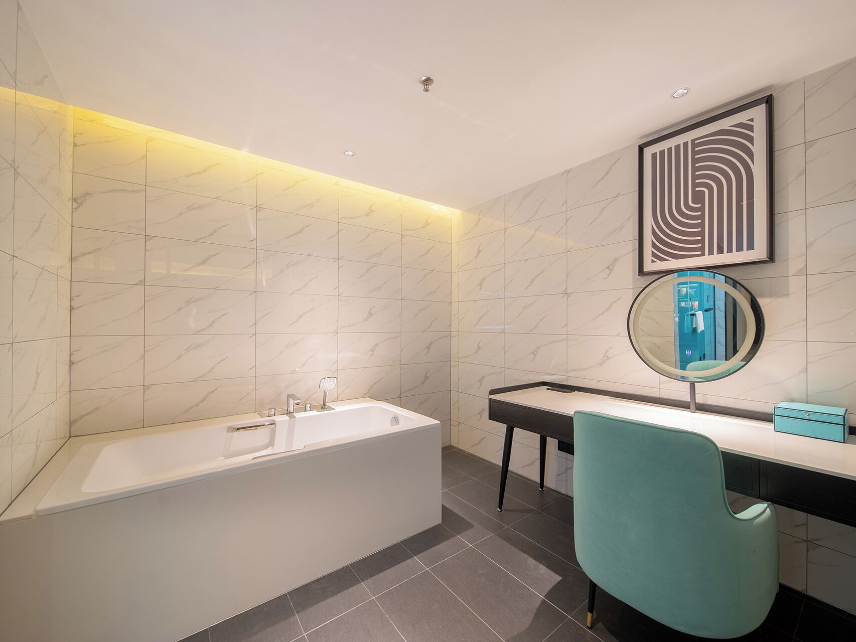 A modern bathroom with a bathtub, a vanity with a mirror, and a teal chair.