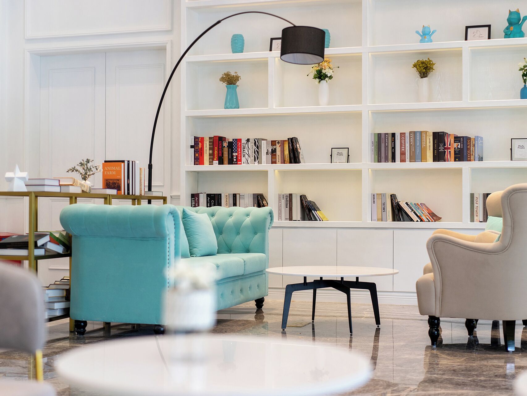 A modern living room with a teal sofa, a white coffee table, and a bookshelf filled with books.