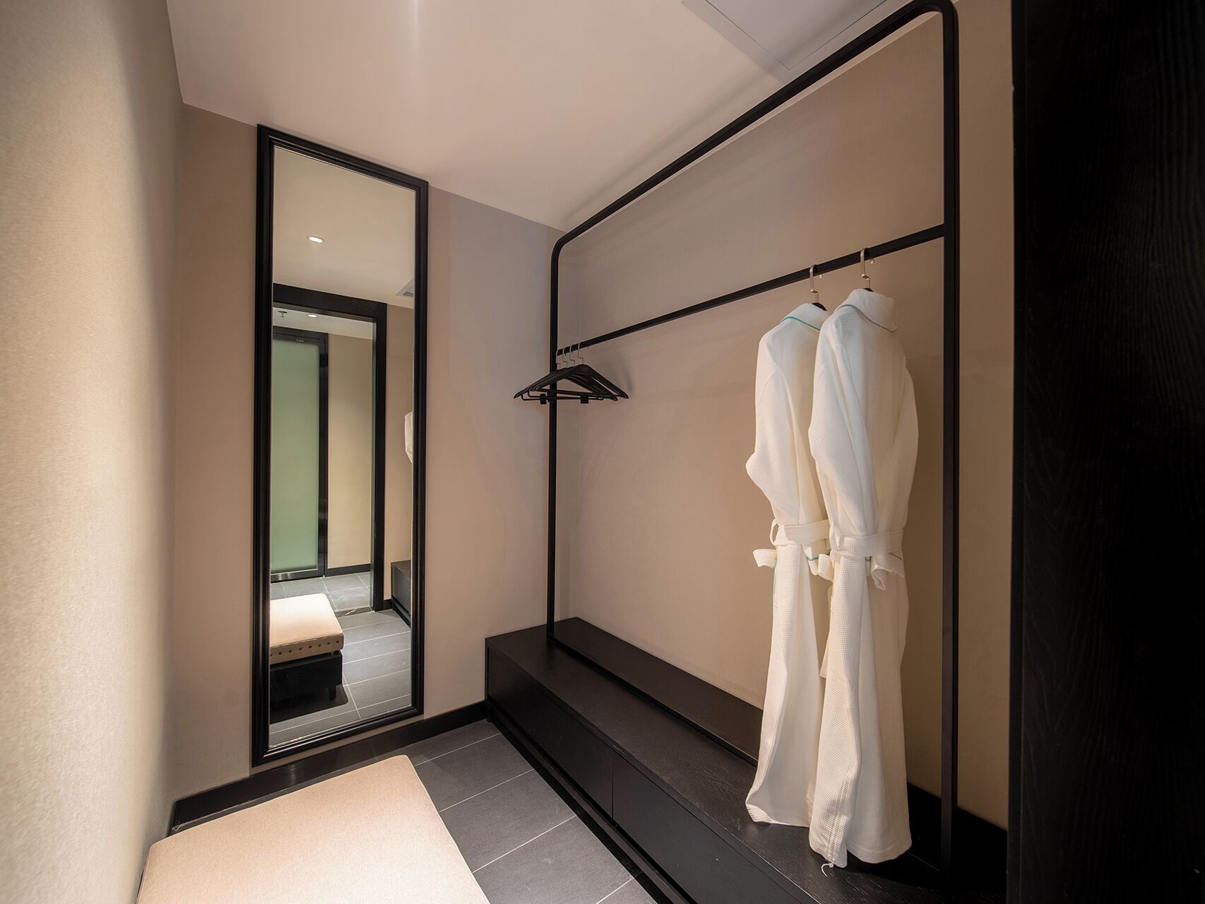 Une salle de bain moderne avec un grand miroir, un porte-serviettes noir et deux peignoirs blancs suspendus.