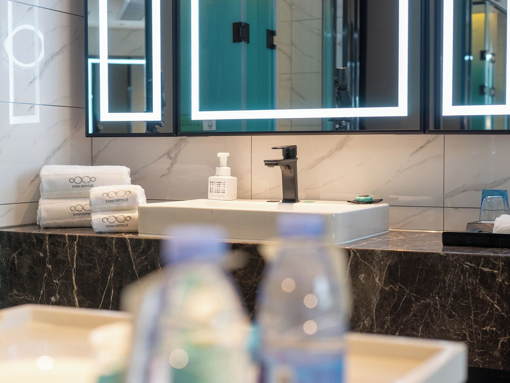 A bathroom with a marble countertop, a sink, a mirror, and a bottle of hand soap.