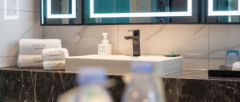 A bathroom with a marble countertop, a sink, a mirror, and a bottle of hand soap.