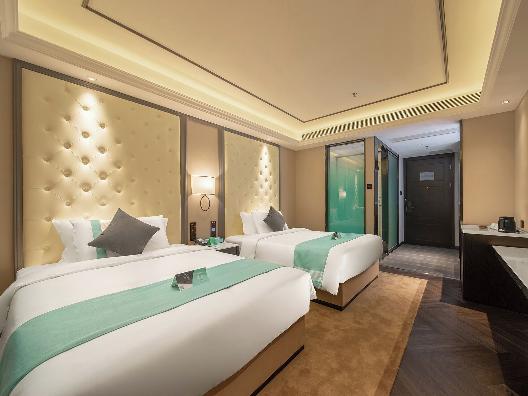 Ein Hotelzimmer mit zwei Betten, einem Schreibtisch und einem durchgegangenen Türrahmen zu sehendem Badezimmer.