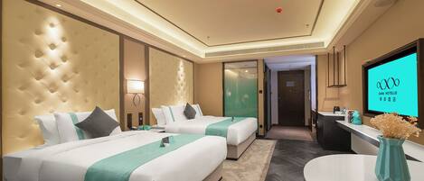 A hotel room with two beds, a desk, a TV, and a reception area.