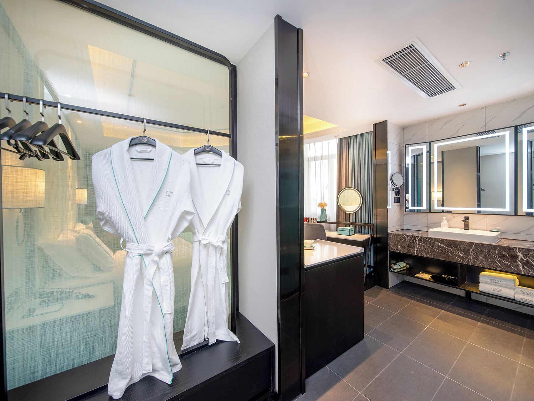 A modern bathroom with a large mirror, a vanity with a marble countertop, and two white robes hanging on a rack.