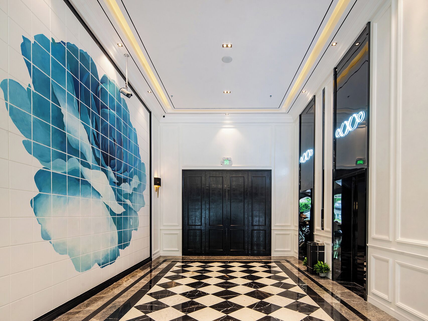 A hallway with a checkered floor, a large blue floral wall mural, and a black door with a neon sign.