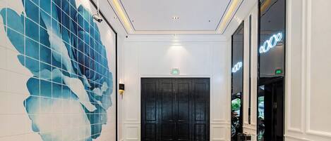 A hallway with a checkered floor, a large blue floral wall mural, and a black door with a neon sign.