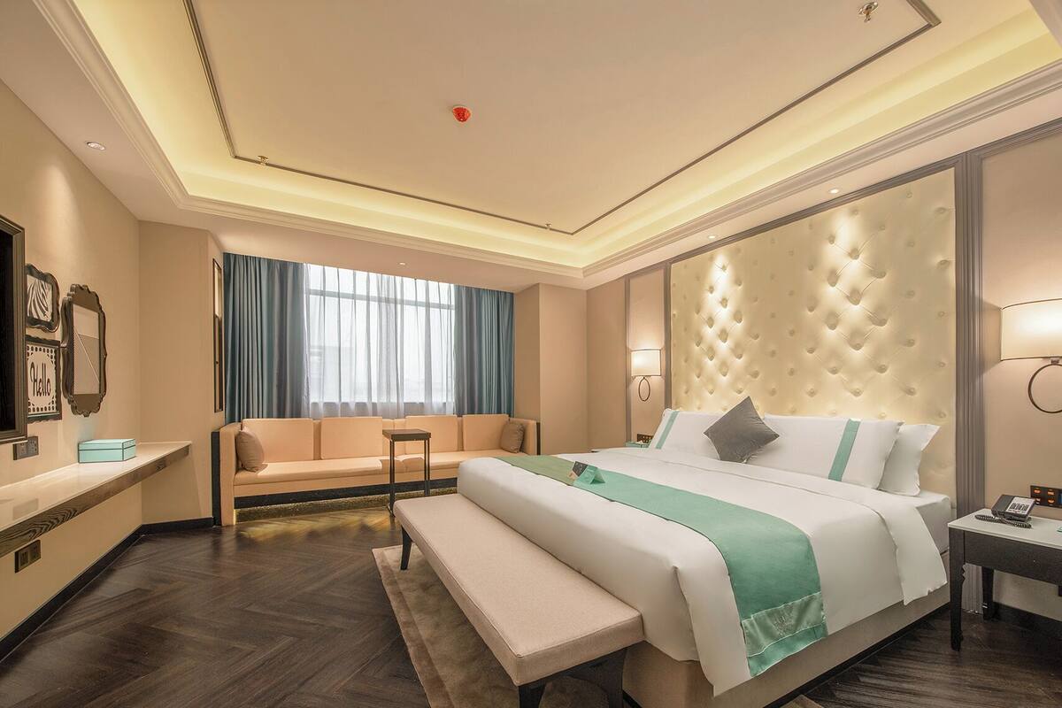 Hotellihuone, jossa on suuri sänky, penkki, sohva, työpöytä ja peili.