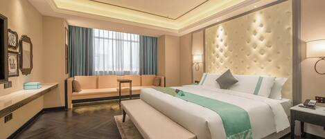 A hotel room with a large bed, a bench, a sofa, a desk, and a mirror.