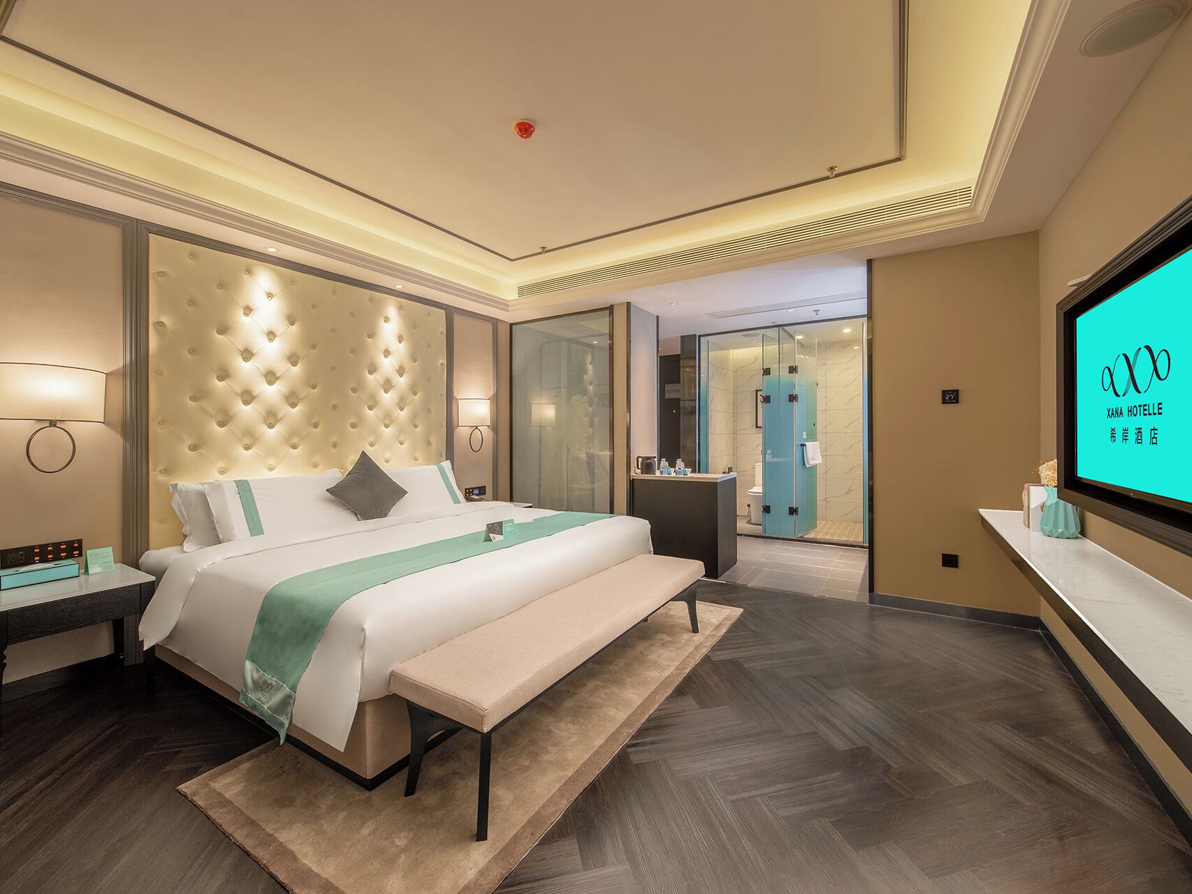 A modern hotel room with a large bed, a bench, a TV, and a glass-enclosed shower area.