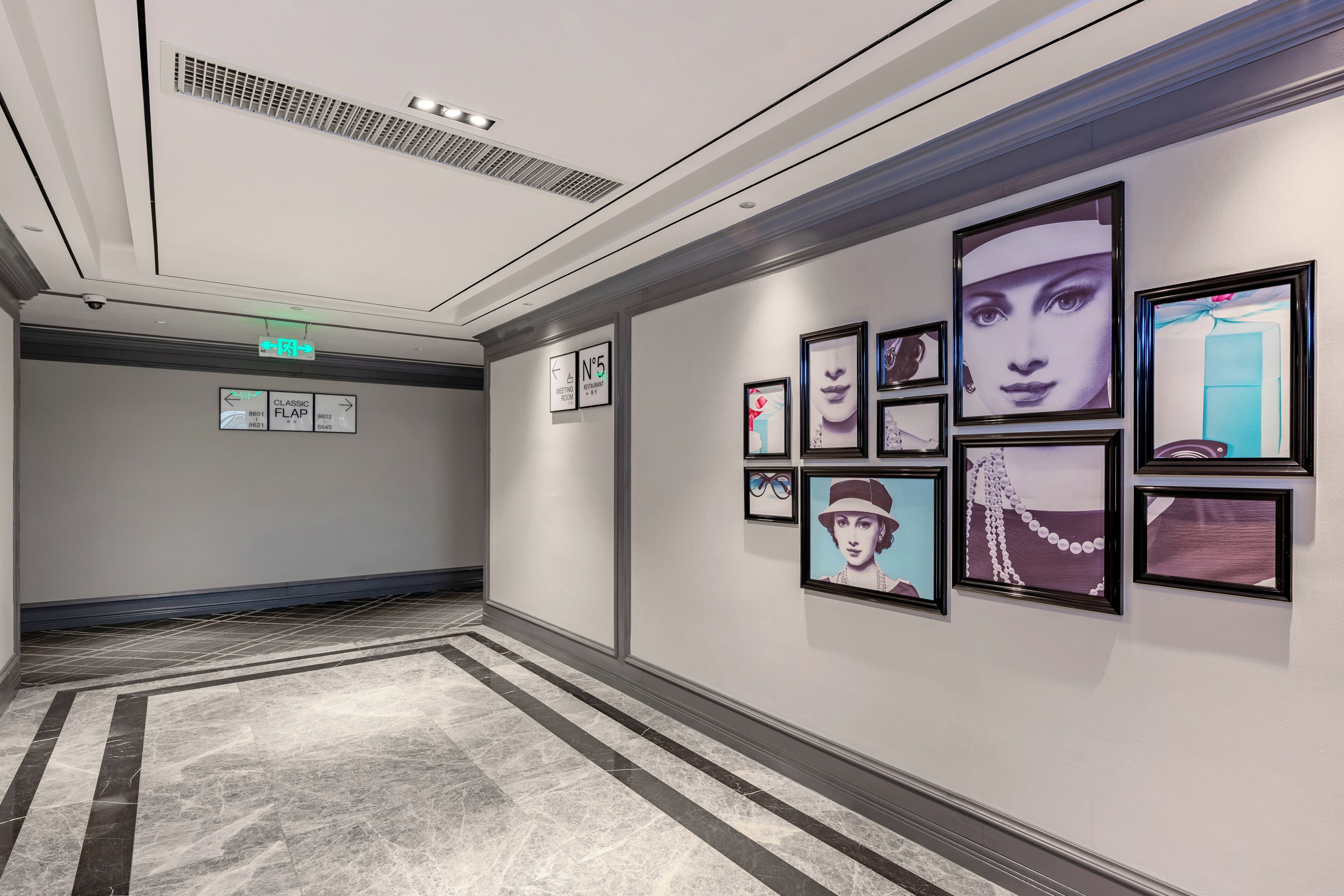 A hallway with directional signs, a tiled floor, and framed artwork on the walls.