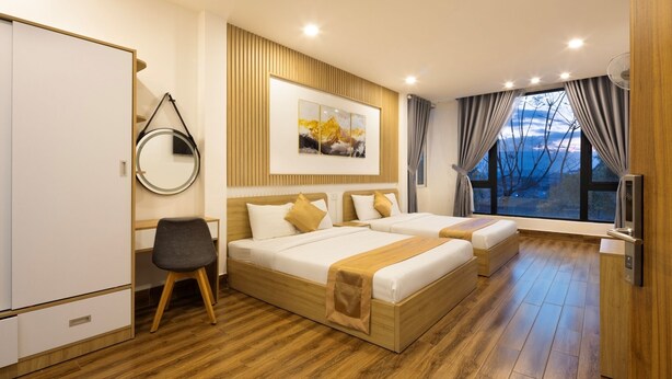 A modern hotel room with two beds, a desk, a chair, a TV, and a large window with a view. - Romance Hotel (Lam Vien - Da Lat)