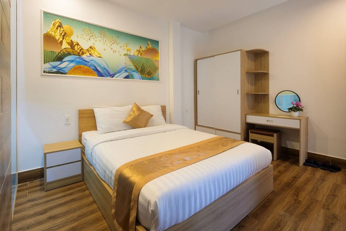 A hotel room with a wooden bed, a desk, a chair, and a large painting on the wall.