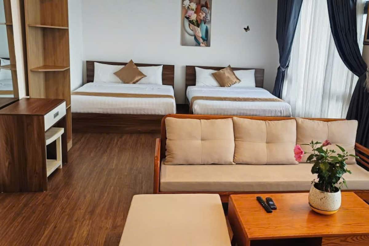 A hotel room with two single beds, a sofa, a wooden coffee table, a small side table, and a potted plant.