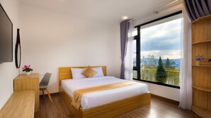 A modern hotel room with a wooden bed, a desk, a chair, and a large window offering a city view. - Romance Hotel (Lam Vien - Da Lat)