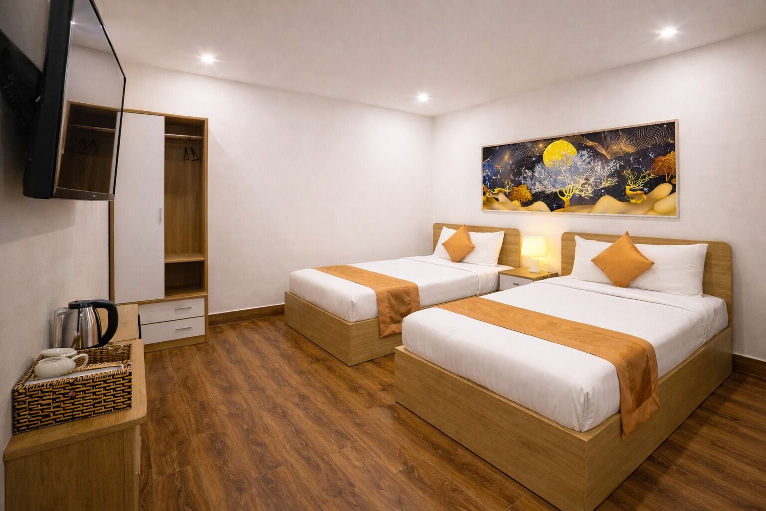 Quarto de hotel com duas camas, piso de madeira, televisão na parede e um quadro sobre as camas.