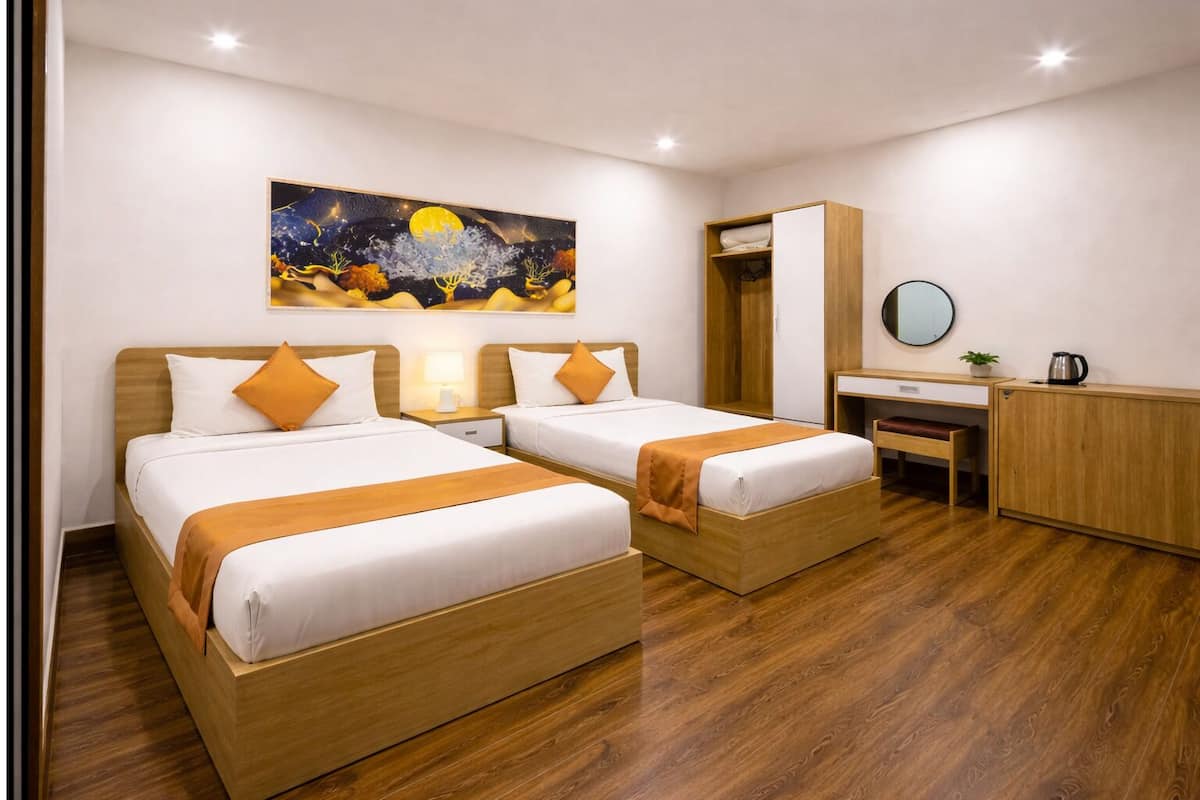 A hotel room with two beds, a desk, a wardrobe, and a painting on the wall.