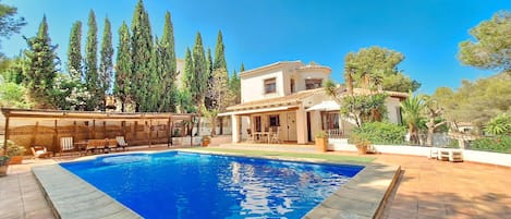 A poolside area with a swimming pool, lounge chairs, and a building with a tiled roof.
