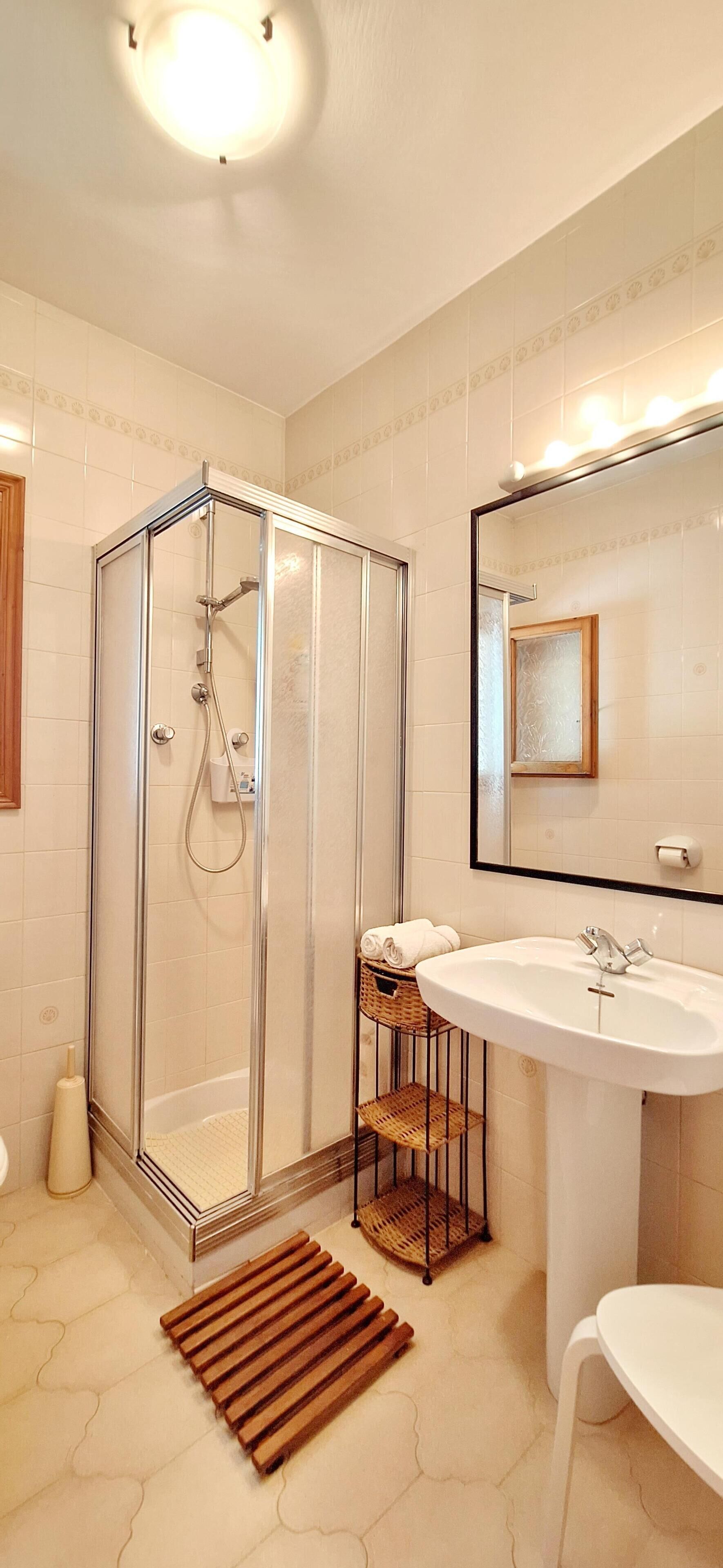 A modern bathroom with a glass-enclosed shower, a white sink, and a large mirror.