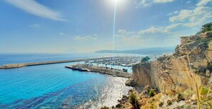 A coastal marina with boats docked, a pier extending into the water, and a rocky cliff in the foreground.