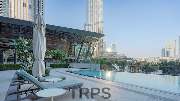 Uma área de piscina no terraço com espreguiçadeiras e um espaço de estar coberto, com vista para um horizonte urbano com edifícios altos.