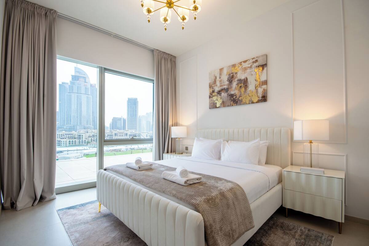 A hotel room with a large bed, two bedside tables, a city view, and a modern chandelier.