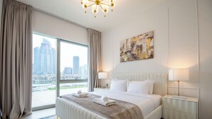Quarto de hotel com uma cama grande, duas mesas de cabeceira, vista para a cidade e um lustre moderno.