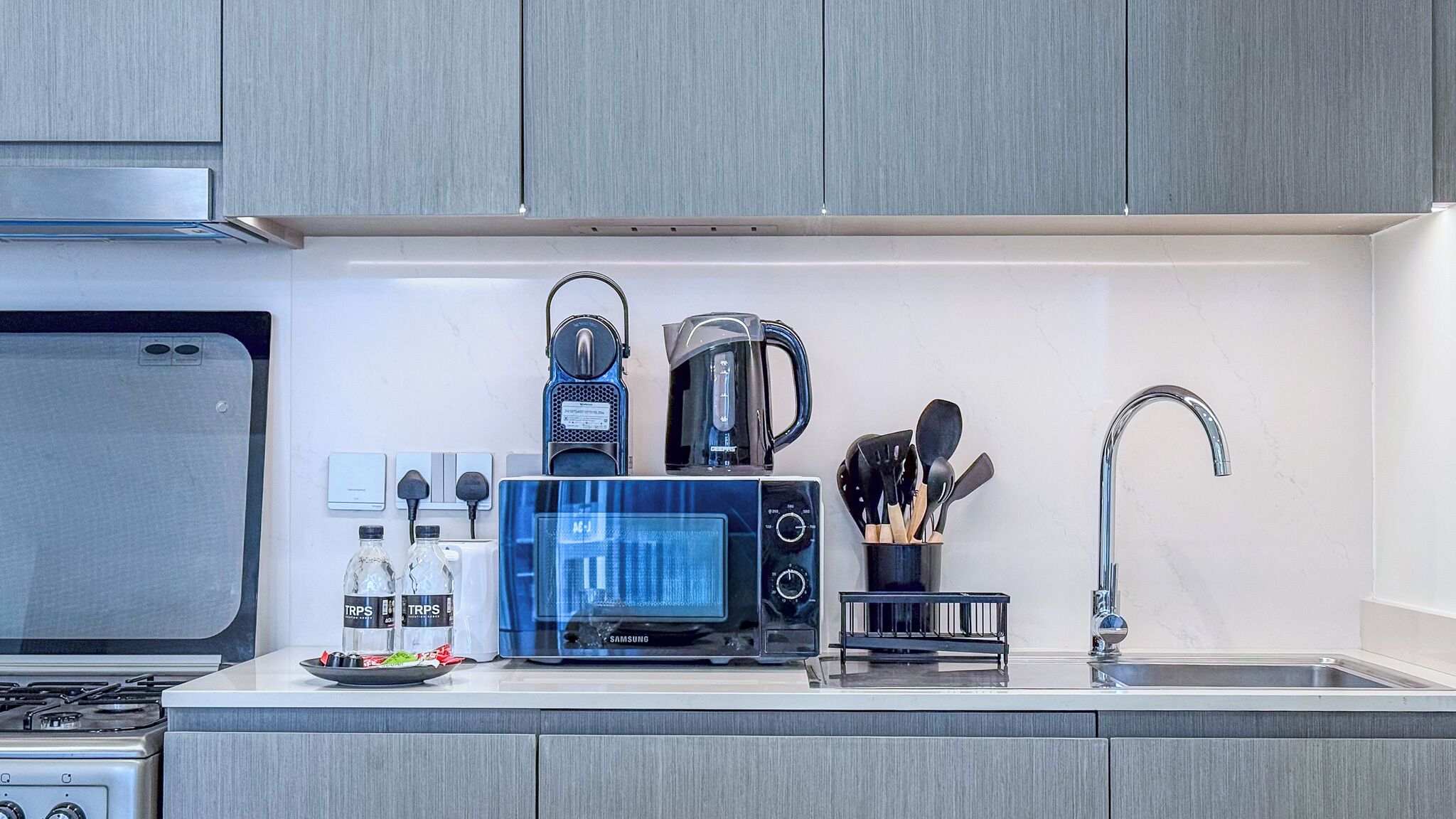 A modern kitchen with a microwave, coffee maker, and utensils on the counter.