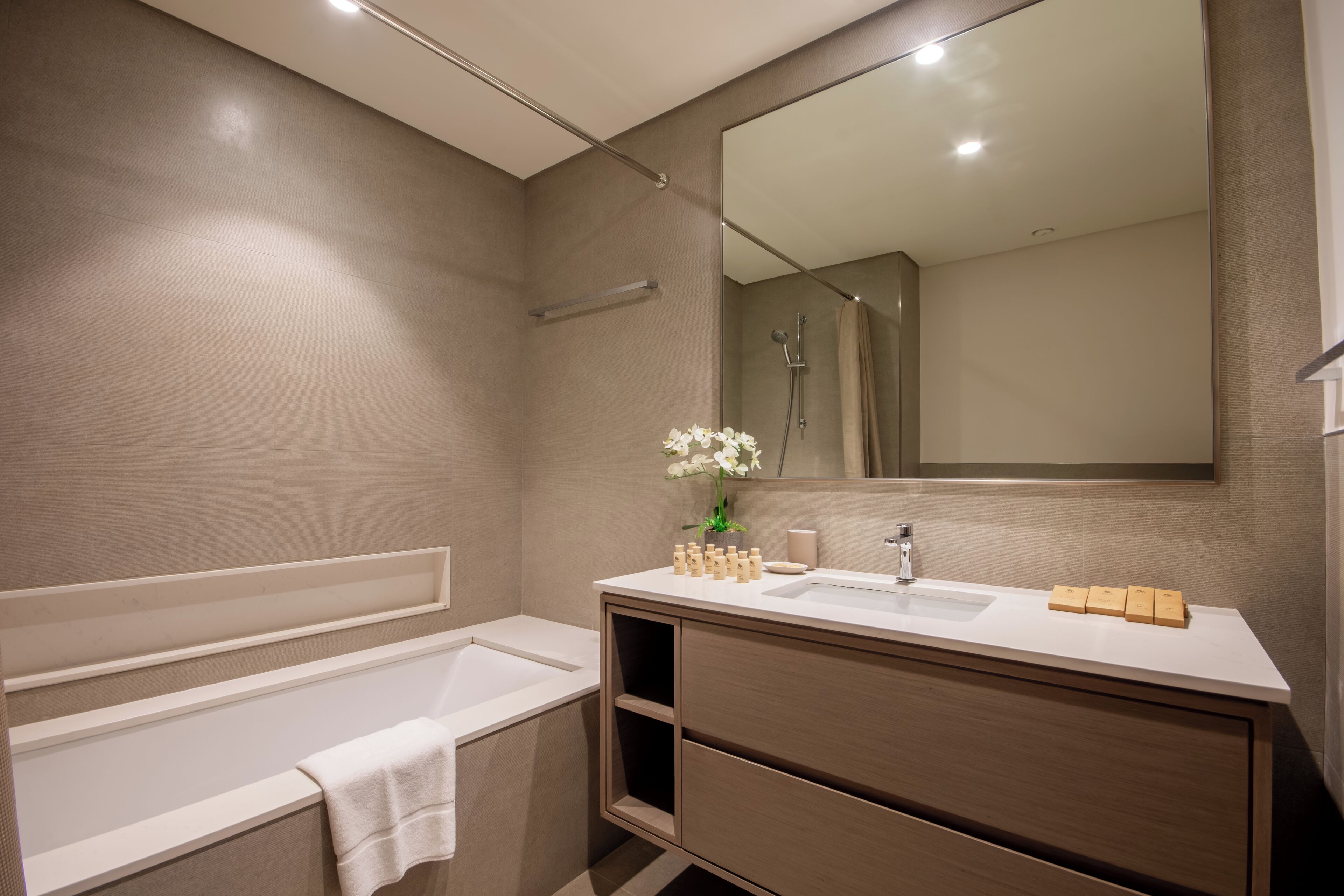 A modern bathroom with a bathtub, a large mirror, and a vanity with a sink and storage.