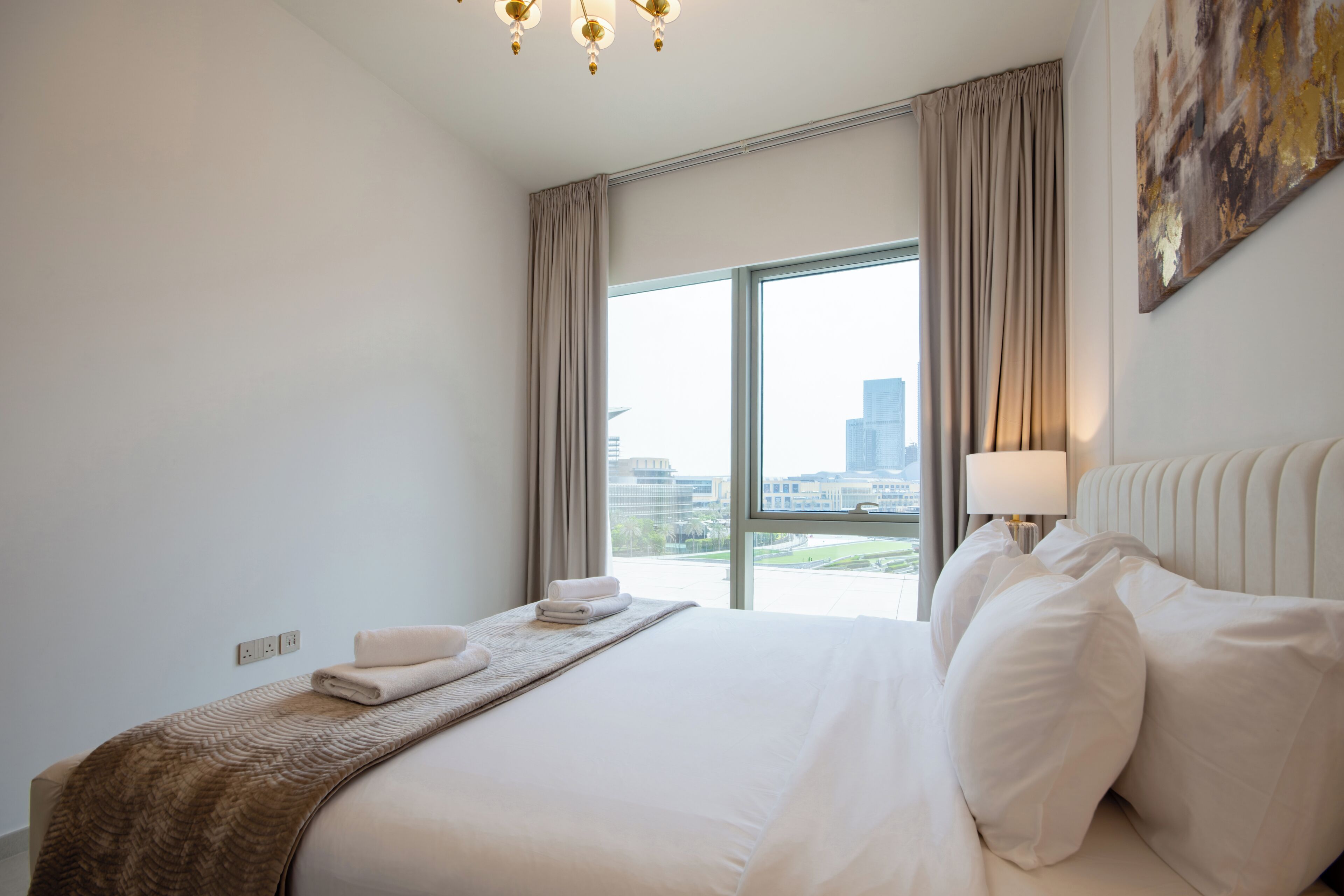 Une chambre d’hôtel avec un grand lit, une table de chevet avec une lampe et une vue sur la ville par une grande fenêtre.