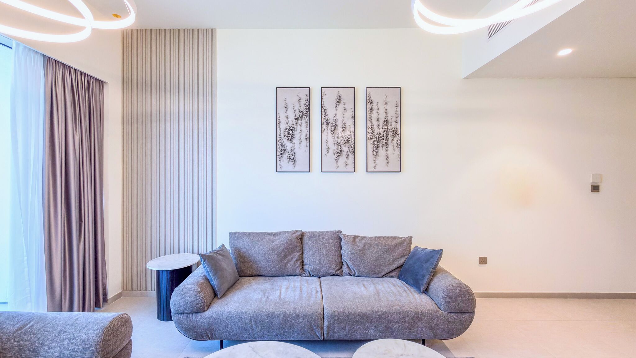 A modern living room with a grey sofa, a round side table, and three abstract wall art pieces.