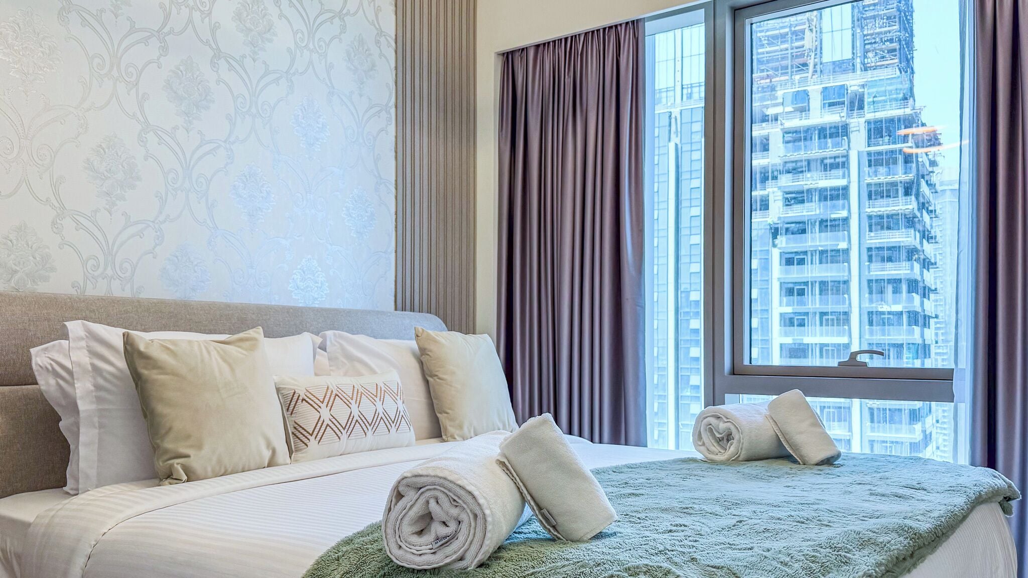 Habitación de hotel con una cama grande, vistas a un paisaje urbano y una ventana con cortinas.