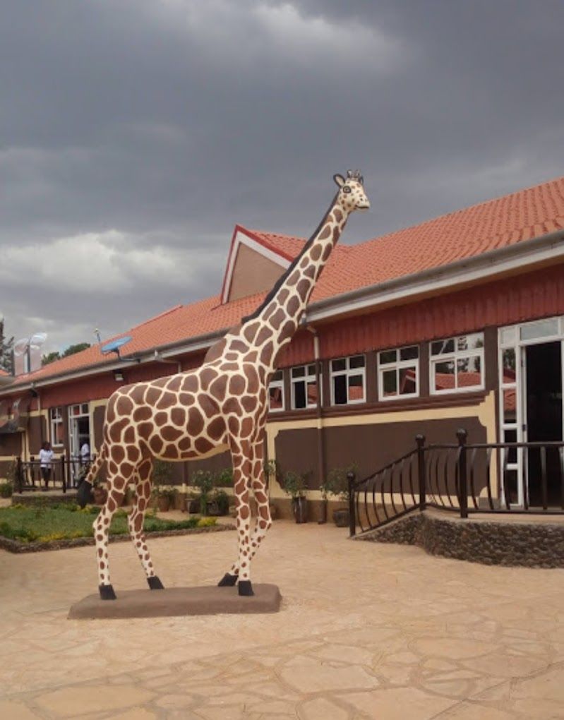A giraffe statue in front of a building with a red roof and multiple windows.
