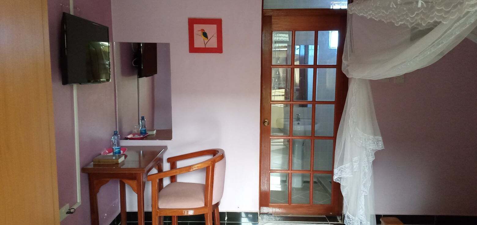 Une pièce comprenant un bureau en bois, une chaise, un téléviseur fixé au mur et une porte à panneaux de verre.