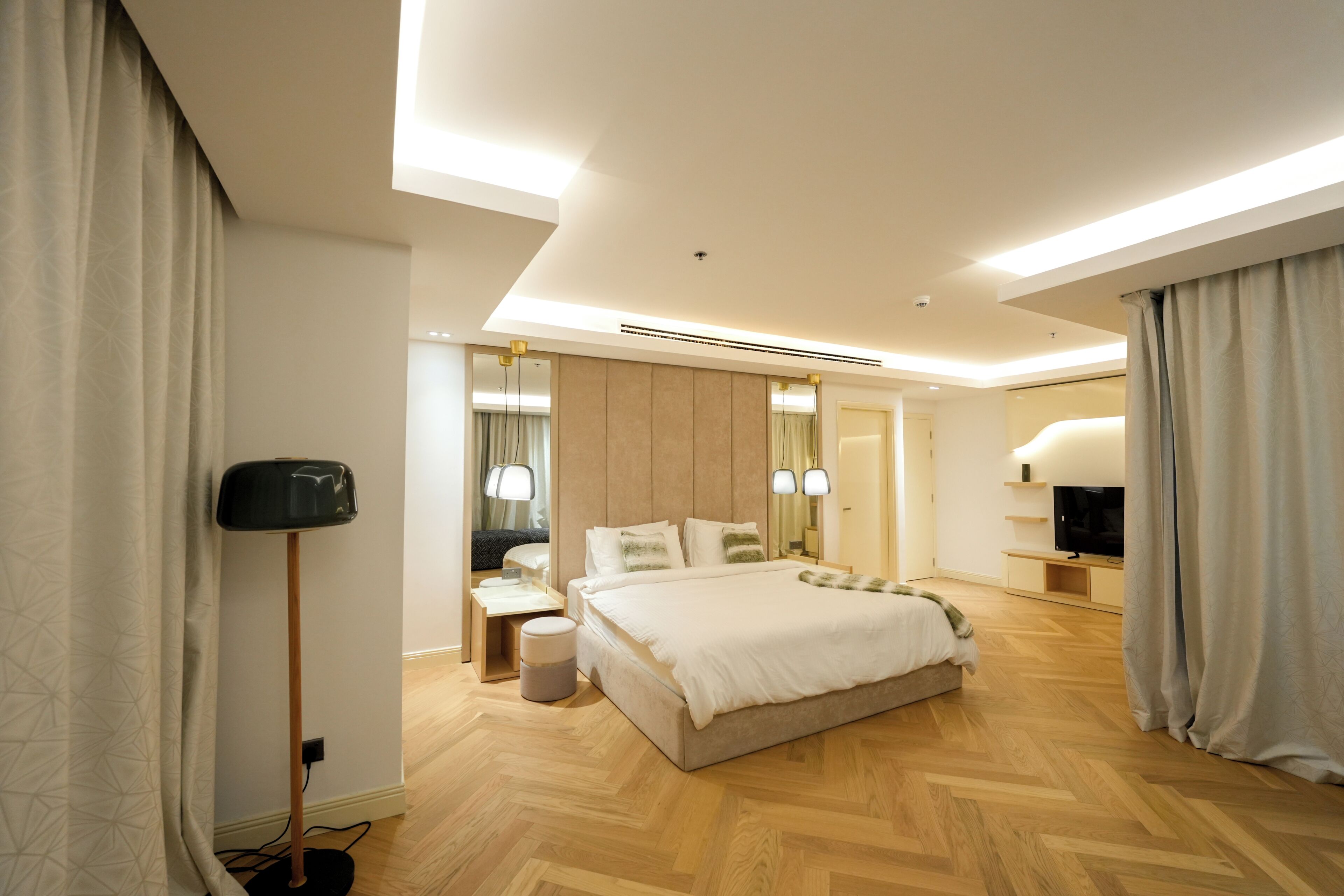 Een moderne hotelkamer met een groot bed, nachtkastjes, een flatscreen televisie en een spiegel.
