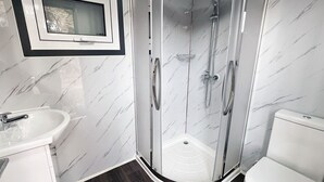 Een moderne badkamer met een douchecabine van glas, een witte wastafel en een toilet.