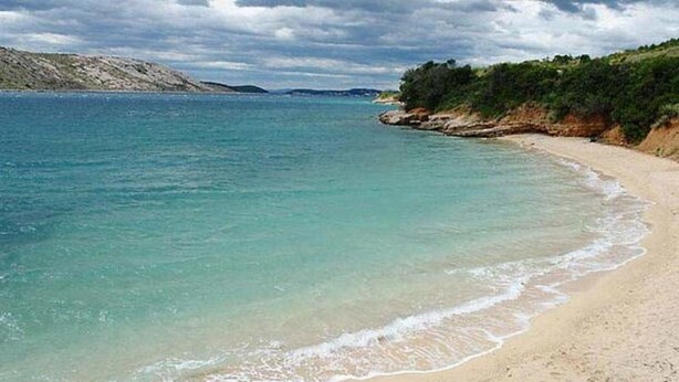 Una spiaggia con acqua cristallina turchese, una costa sabbiosa e scogliere rocciose sullo sfondo.