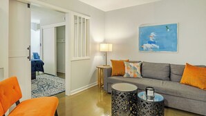 Una sala de estar moderna con un sofá gris, cojines naranjas, una alfombra estampada y un cuadro en la pared.