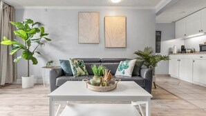 Un salon moderne avec un canapé gris, une table basse blanche et un coin cuisine doté de meubles blancs.