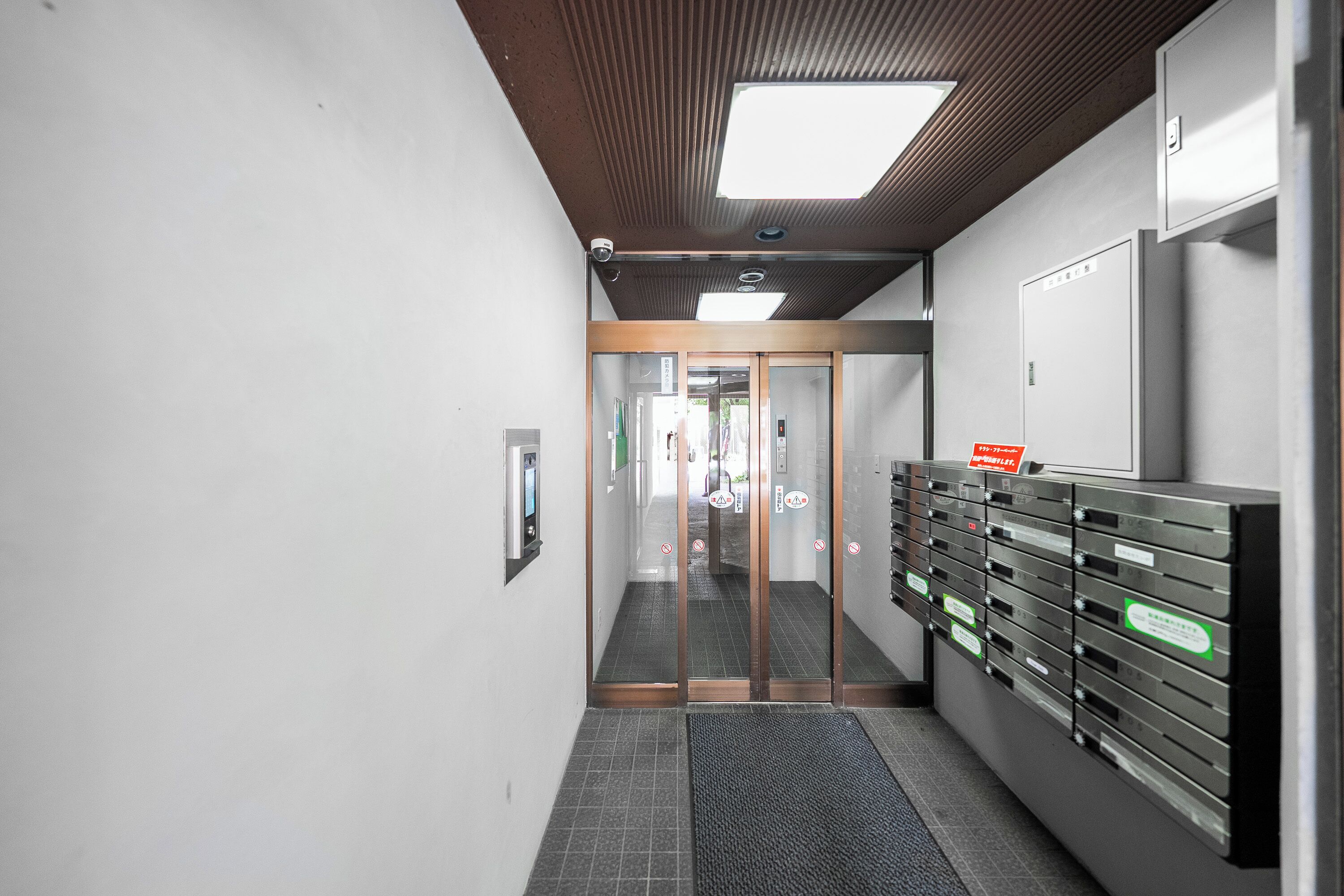 A hallway with a glass door, a security camera, and a row of mailboxes.
