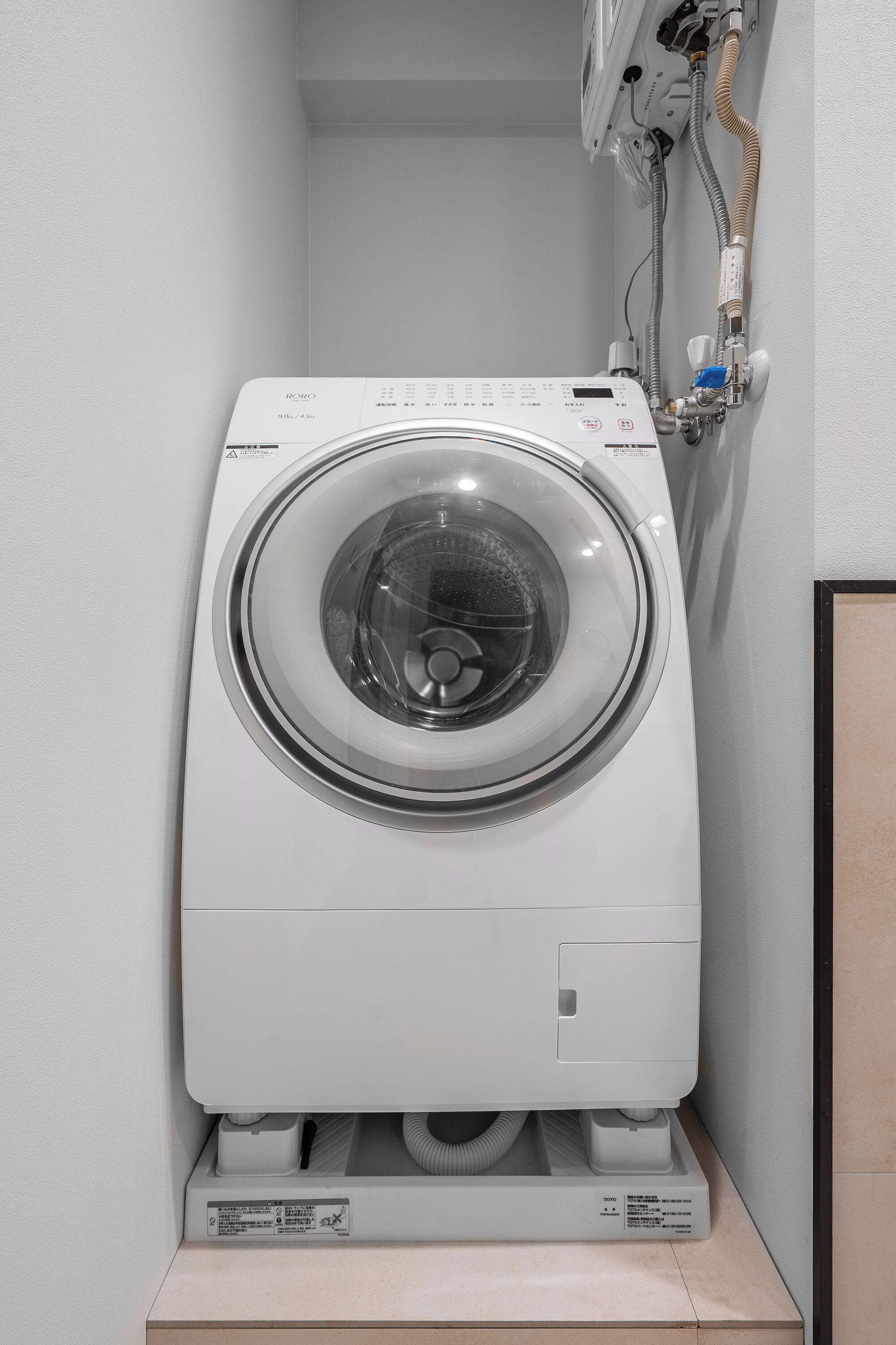 Une machine à laver à chargement frontal, dotée d’un panneau de commande, placée sur un socle.