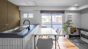 Et moderne køkken med en indbygget ø, et spiseområde med bord og stole, en potteplante og udsigt over byen gennem store vinduer.