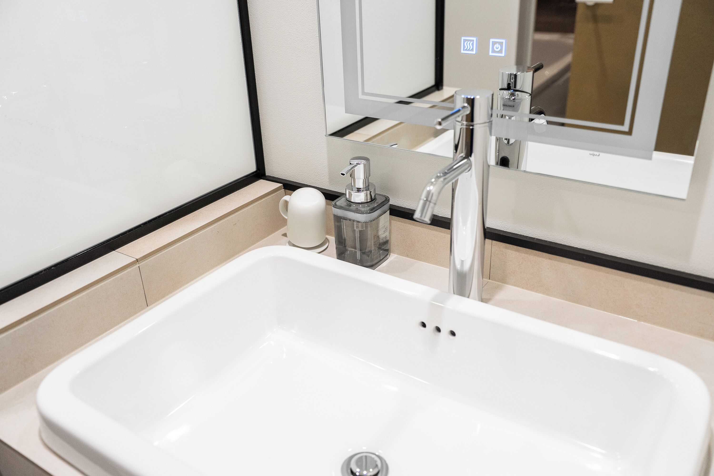 A white bathroom sink with a modern faucet, a soap dispenser, and a cup holder.