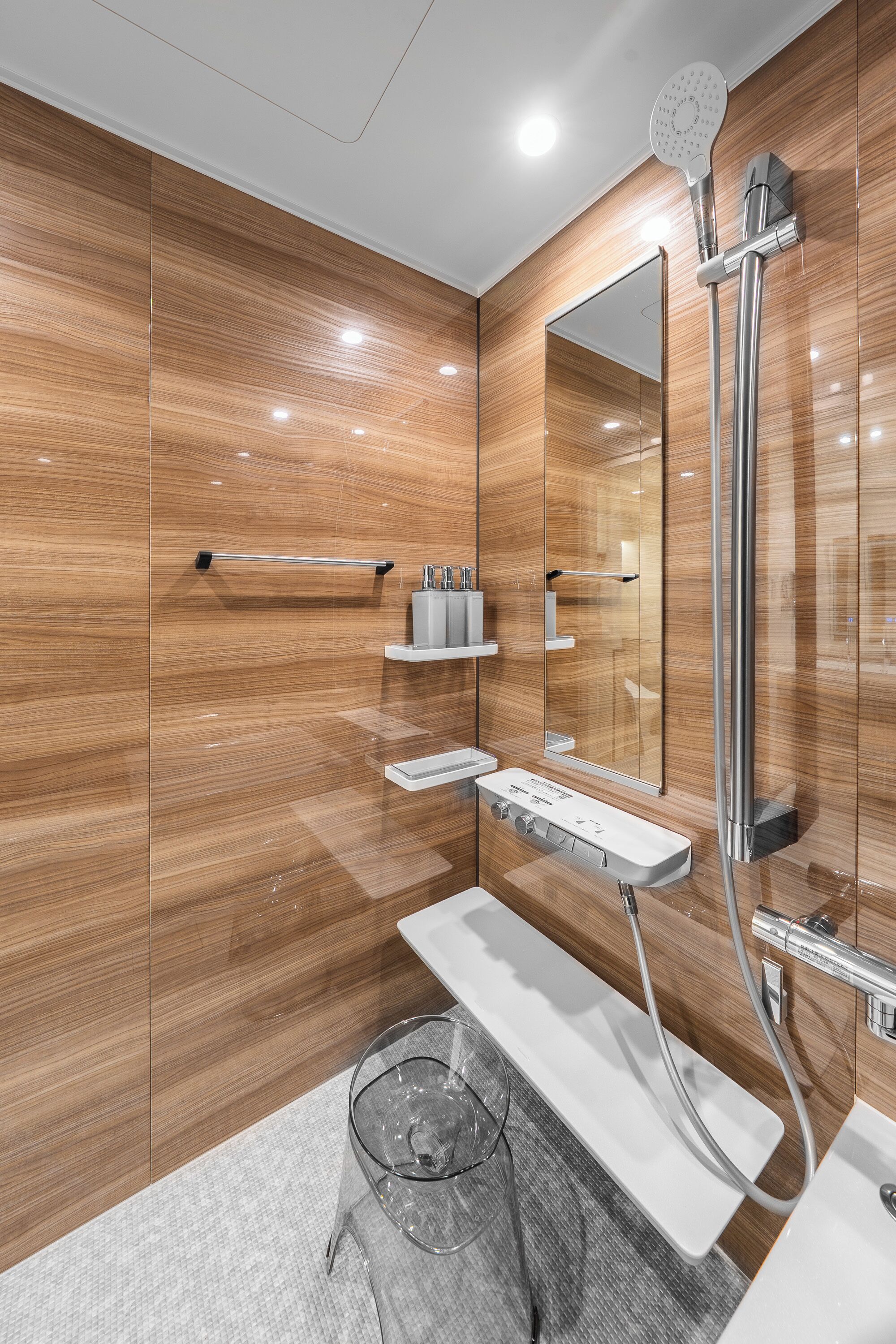 A modern bathroom with a wooden wall, a large mirror, a shower, and a vanity with a sink and towel rack.