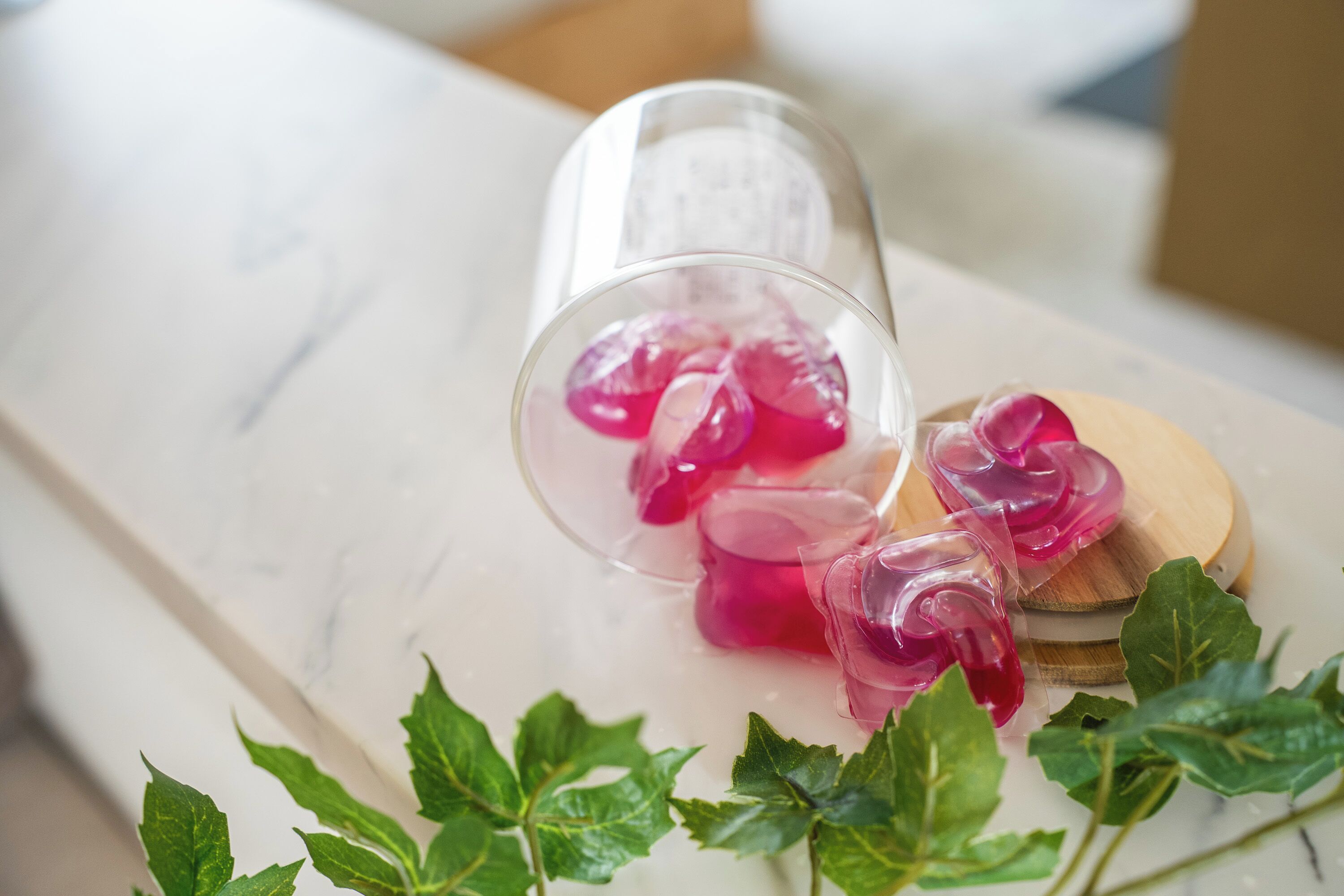 Une bouteille en verre transparent contenant un liquide rose, posée sur une surface en marbre et entourée de feuilles vertes.