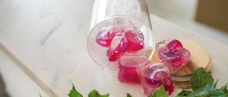Une bouteille en verre transparent contenant un liquide rose, posée sur une surface en marbre et entourée de feuilles vertes.