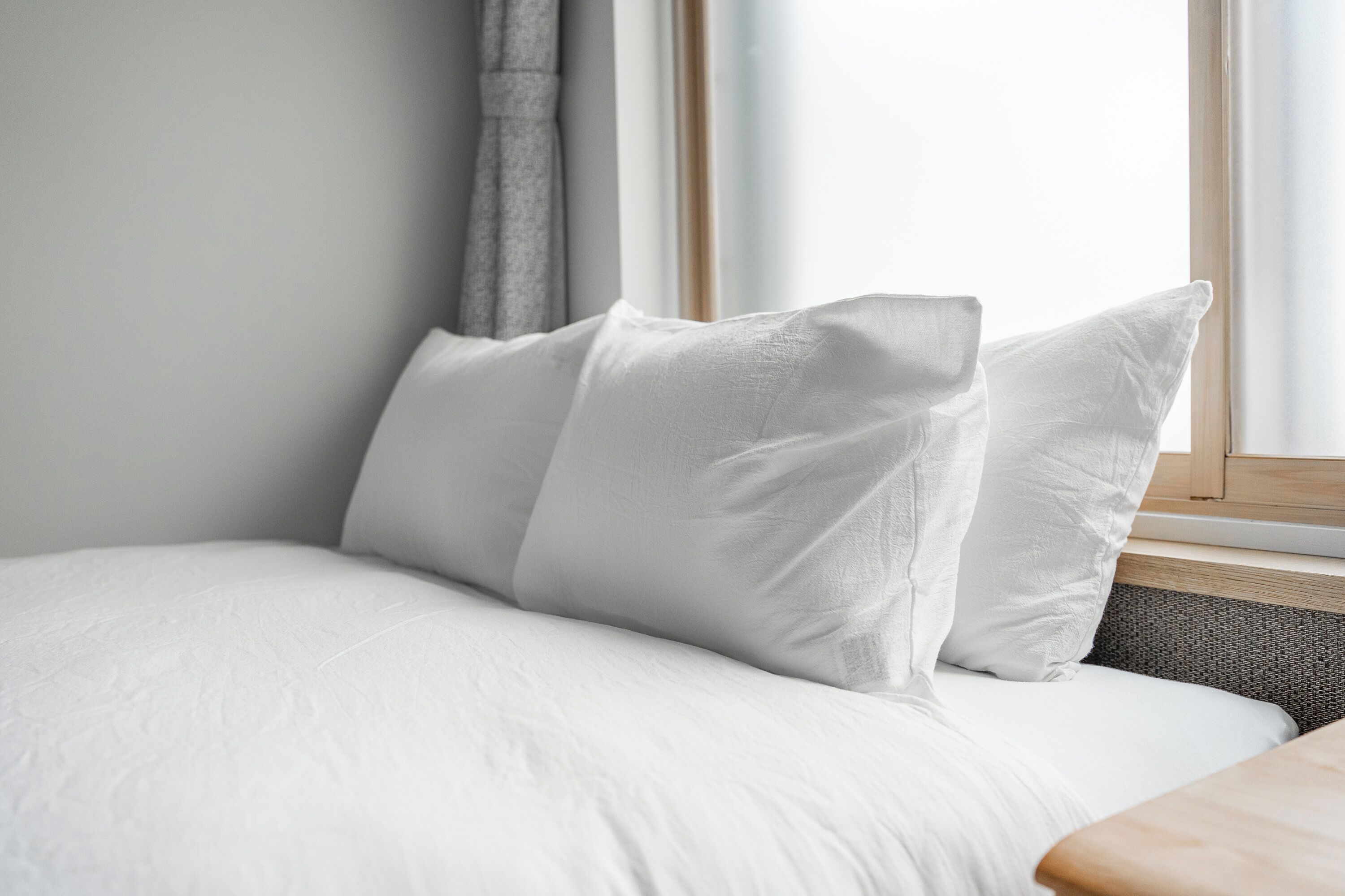 Una cama bien hecha con ropa blanca y almohadas, ubicada junto a una ventana con vistas al exterior.