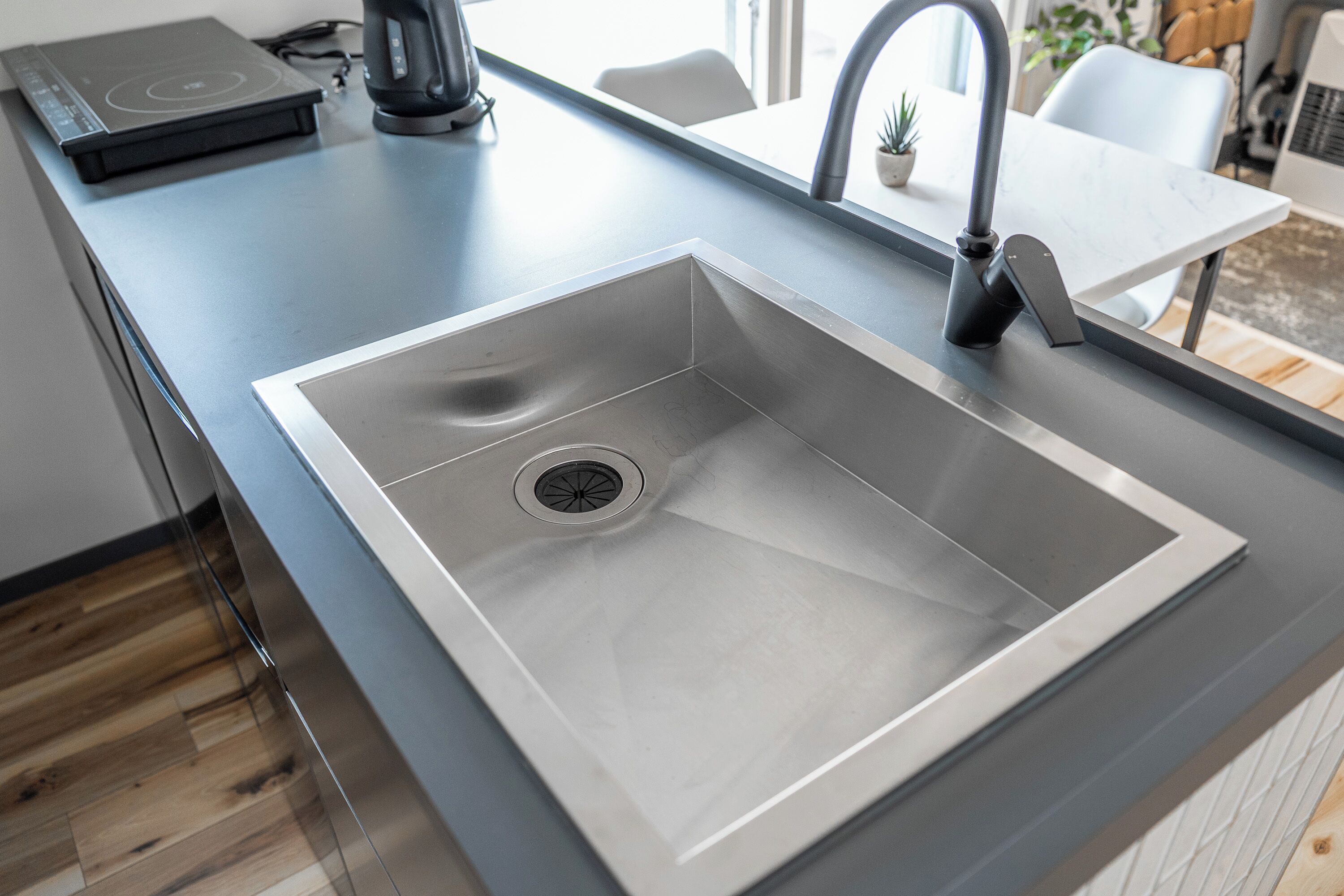A modern kitchen with a stainless steel sink, a coffee maker, and a tablet on the counter.