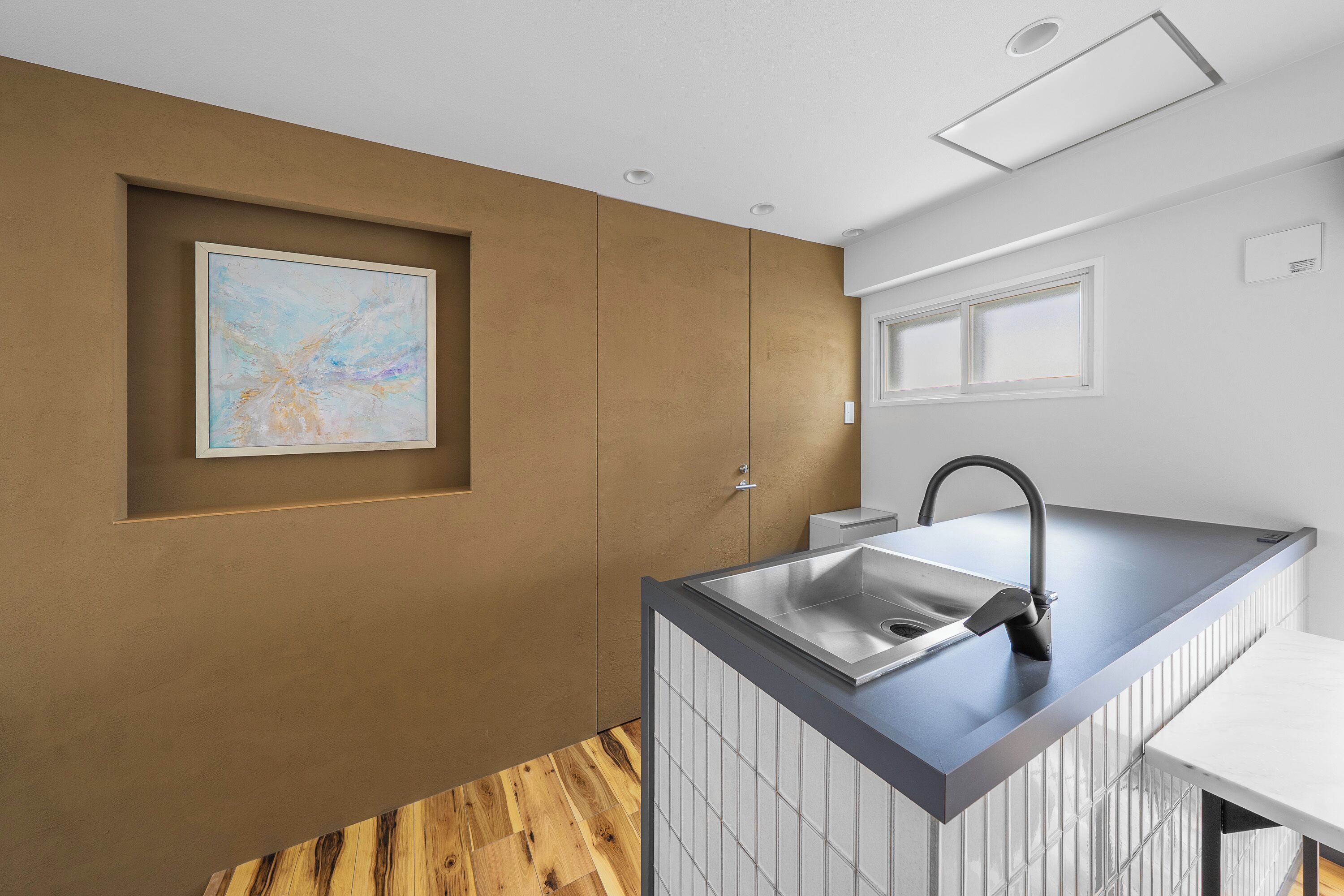 A modern kitchen with a built-in sink, wooden flooring, and a recessed ceiling light.